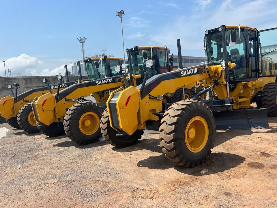 Row of yellow motor graders and wheel loaders on a cargo yard