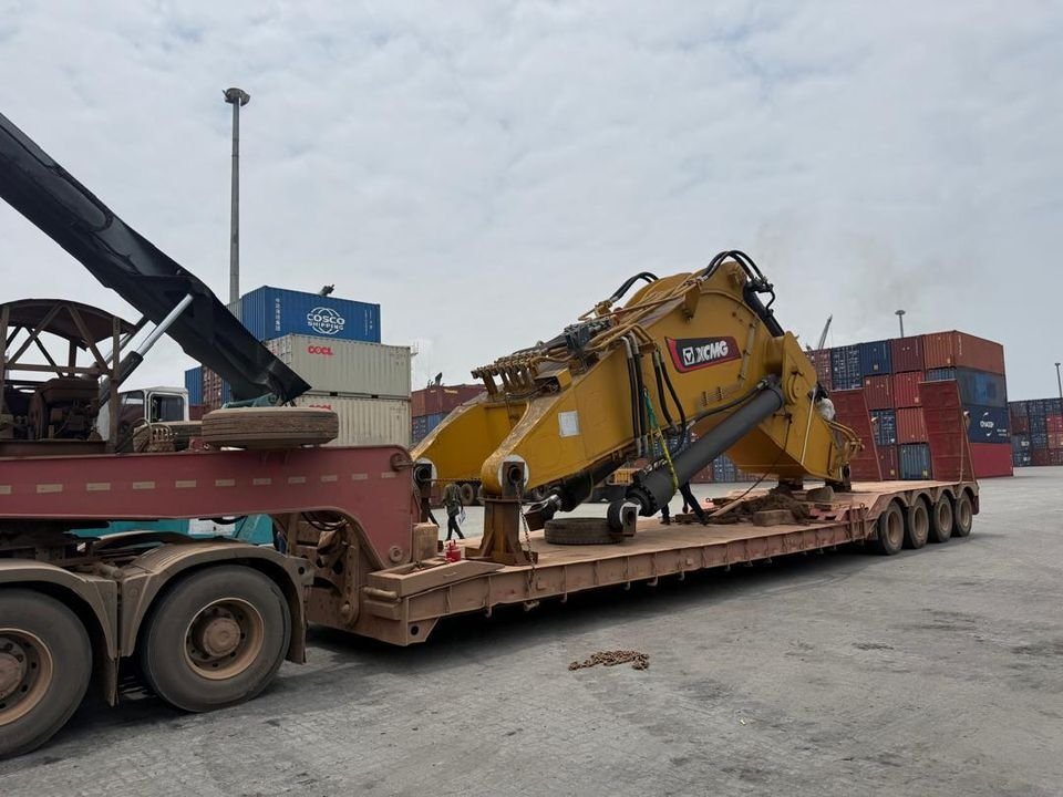 Yellow XCMG excavator boom and arm secured on a red lowbed trailer in a container yard