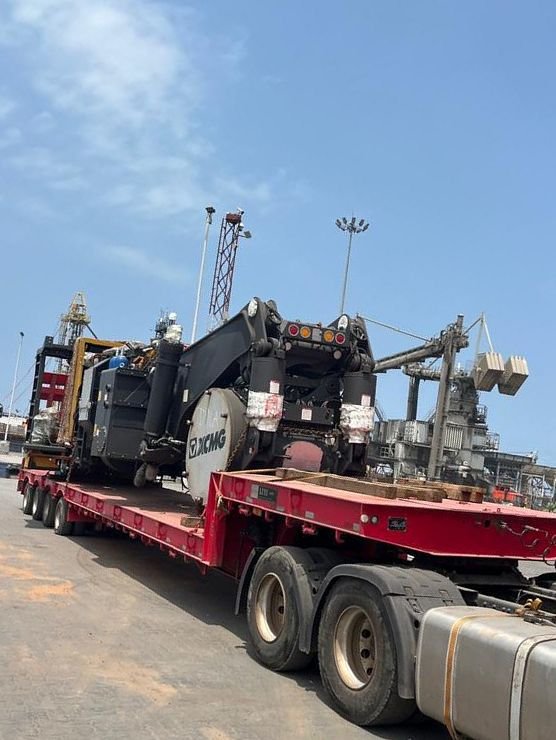 XCMG heavy machine loaded on a red lowbed trailer behind a tractor unit at the port